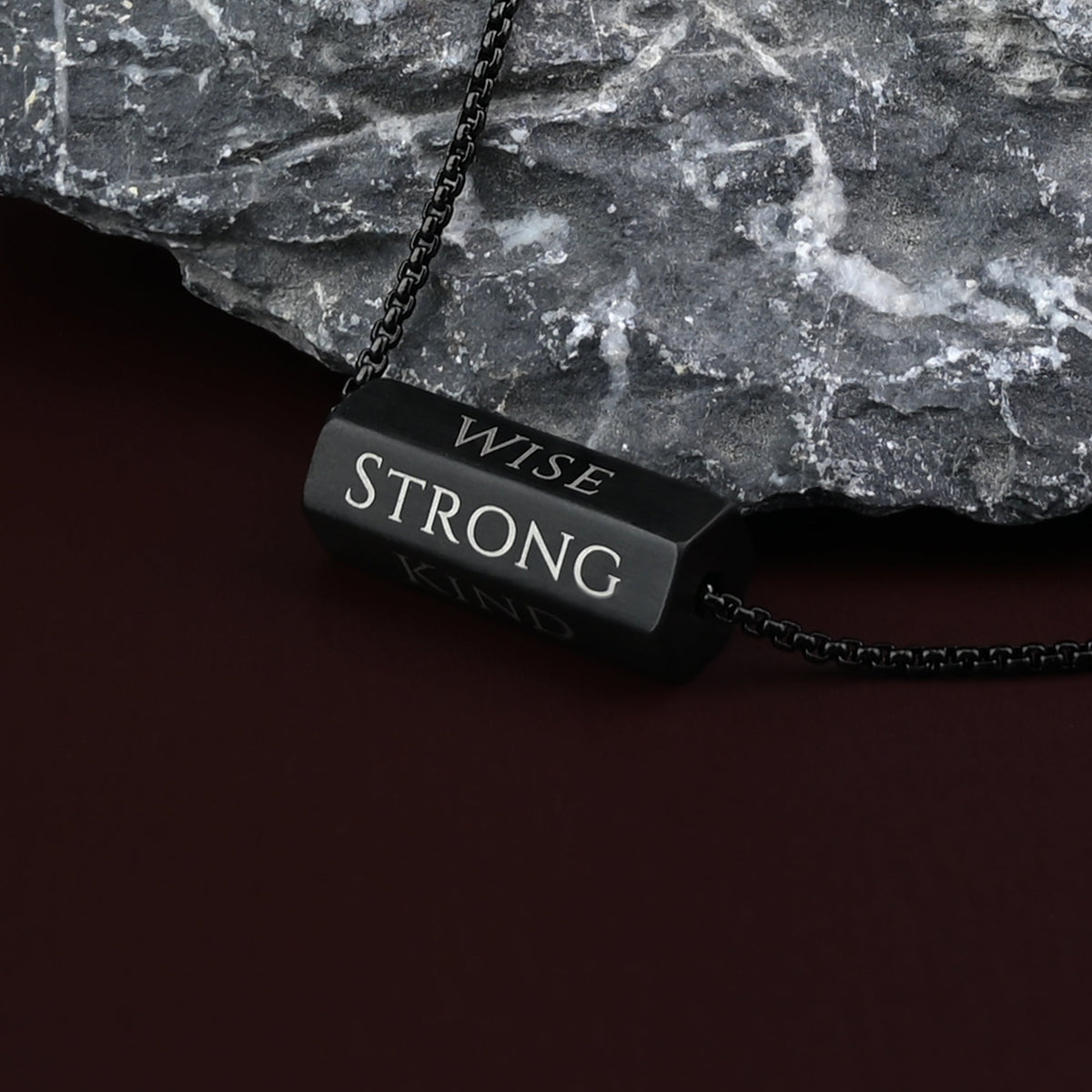 Close-up of Pillar matte black bar engraved Wise and Strong against gray stone