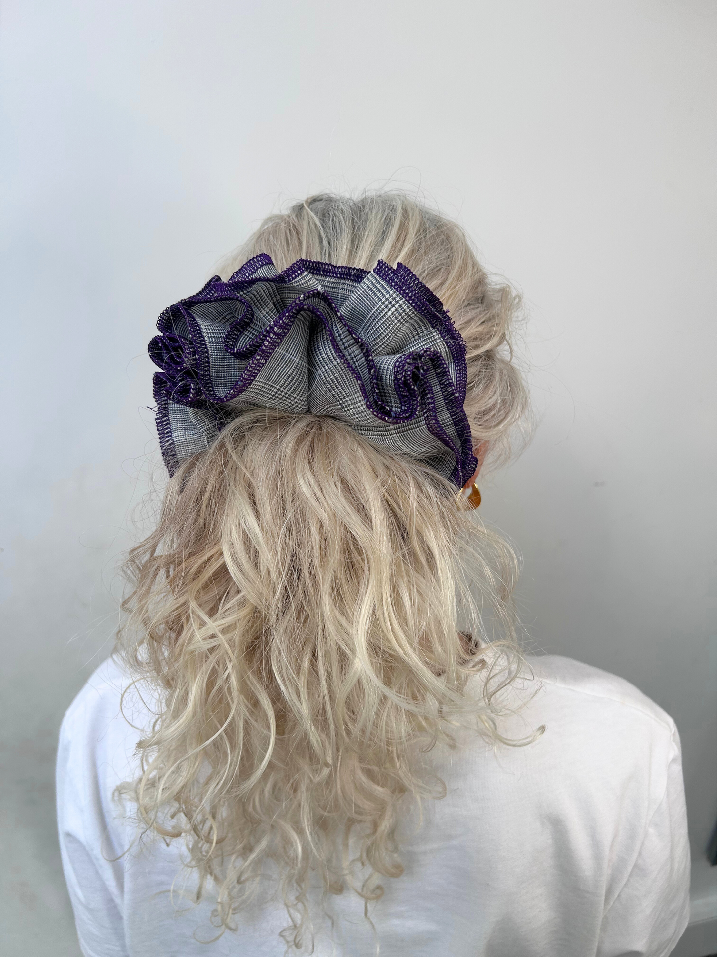 Person with curly blonde hair wearing a decorative purple hair clip against a plain background