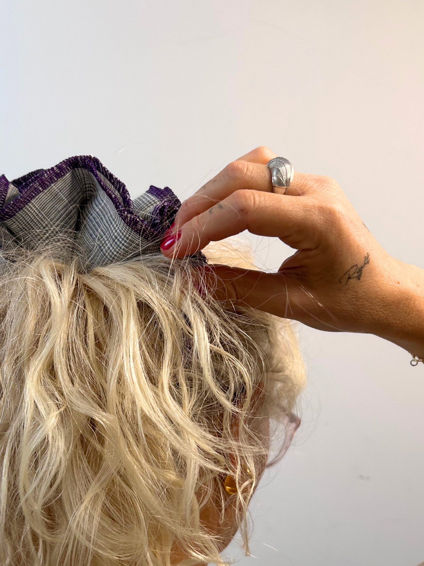 Person adjusting a grey hair scrunchie wearing a silver ring against a plain background
