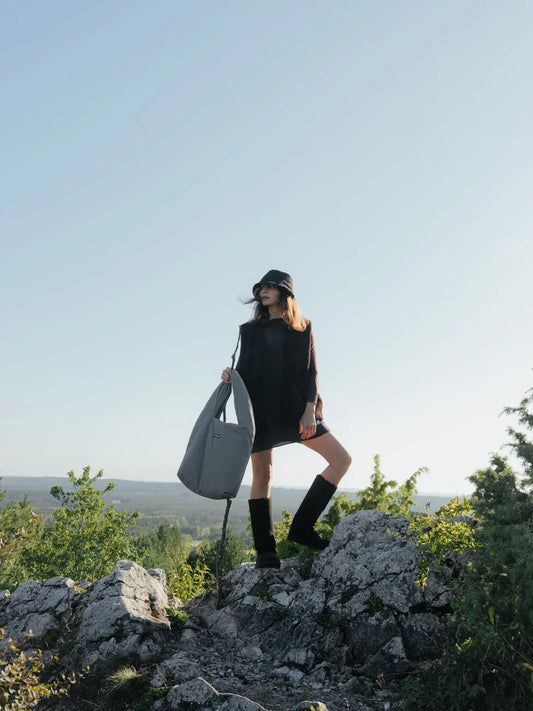 Person holding a gray bag on a rocky outcrop with a scenic background wearing long vegan boots