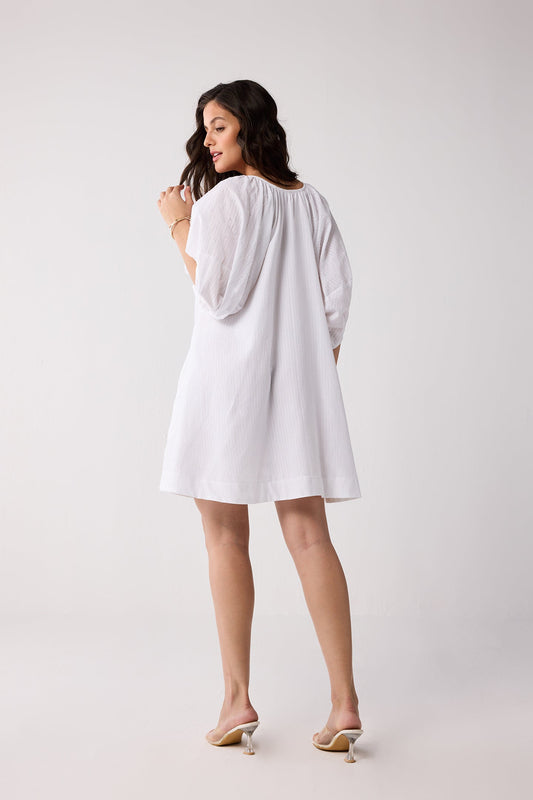 A woman wearing a white dress on a plain background.