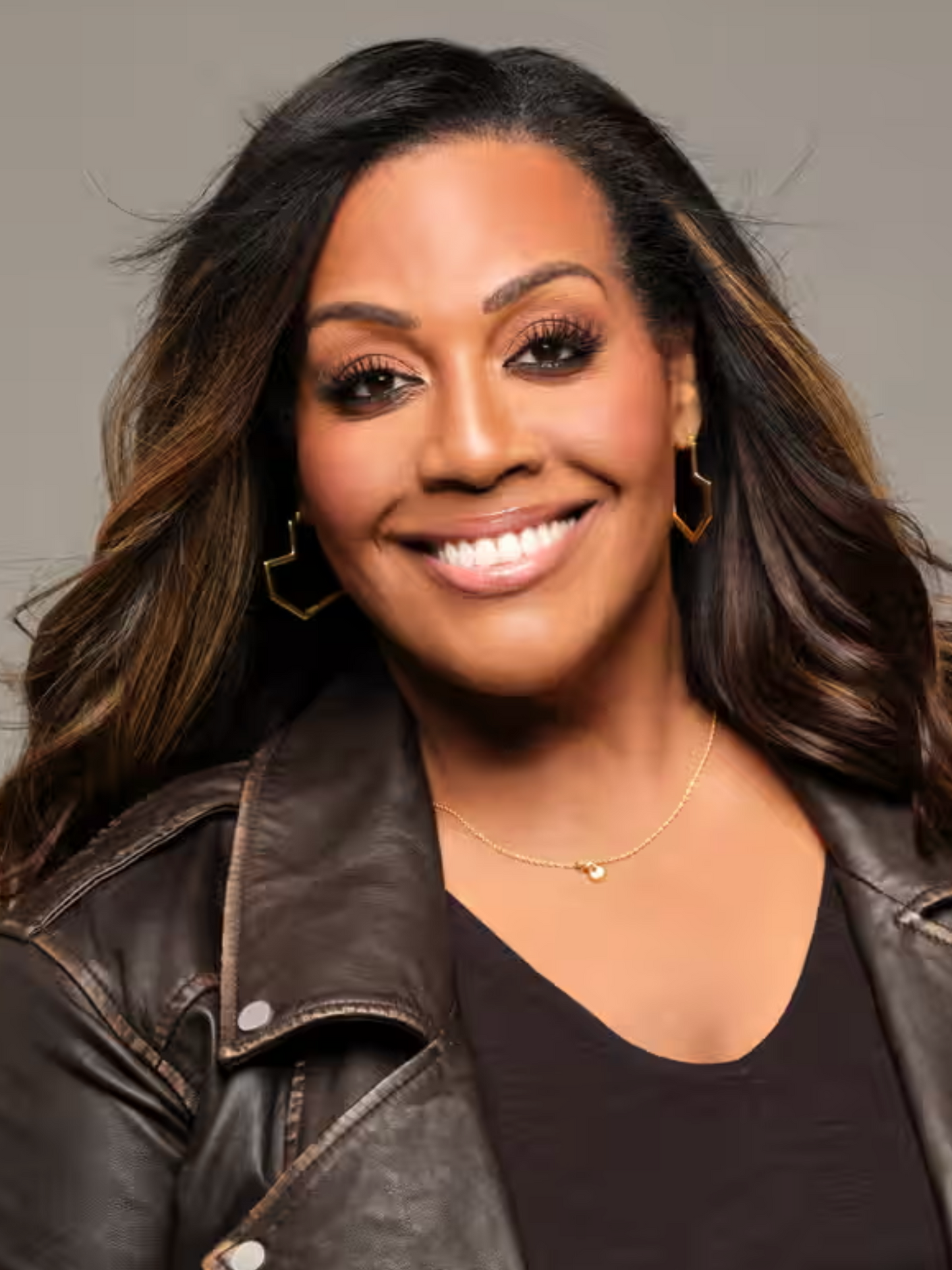 Alison Hammond wearing a black leather jacket with gold heart hoop earrings against a grey background