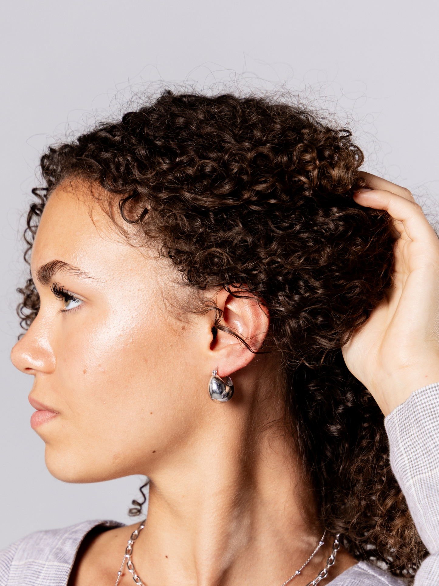 Woman wearing silver ball hoop earrings against a neutral background