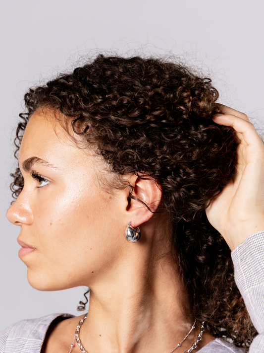 Woman wearing silver ball hoop earrings against a neutral background