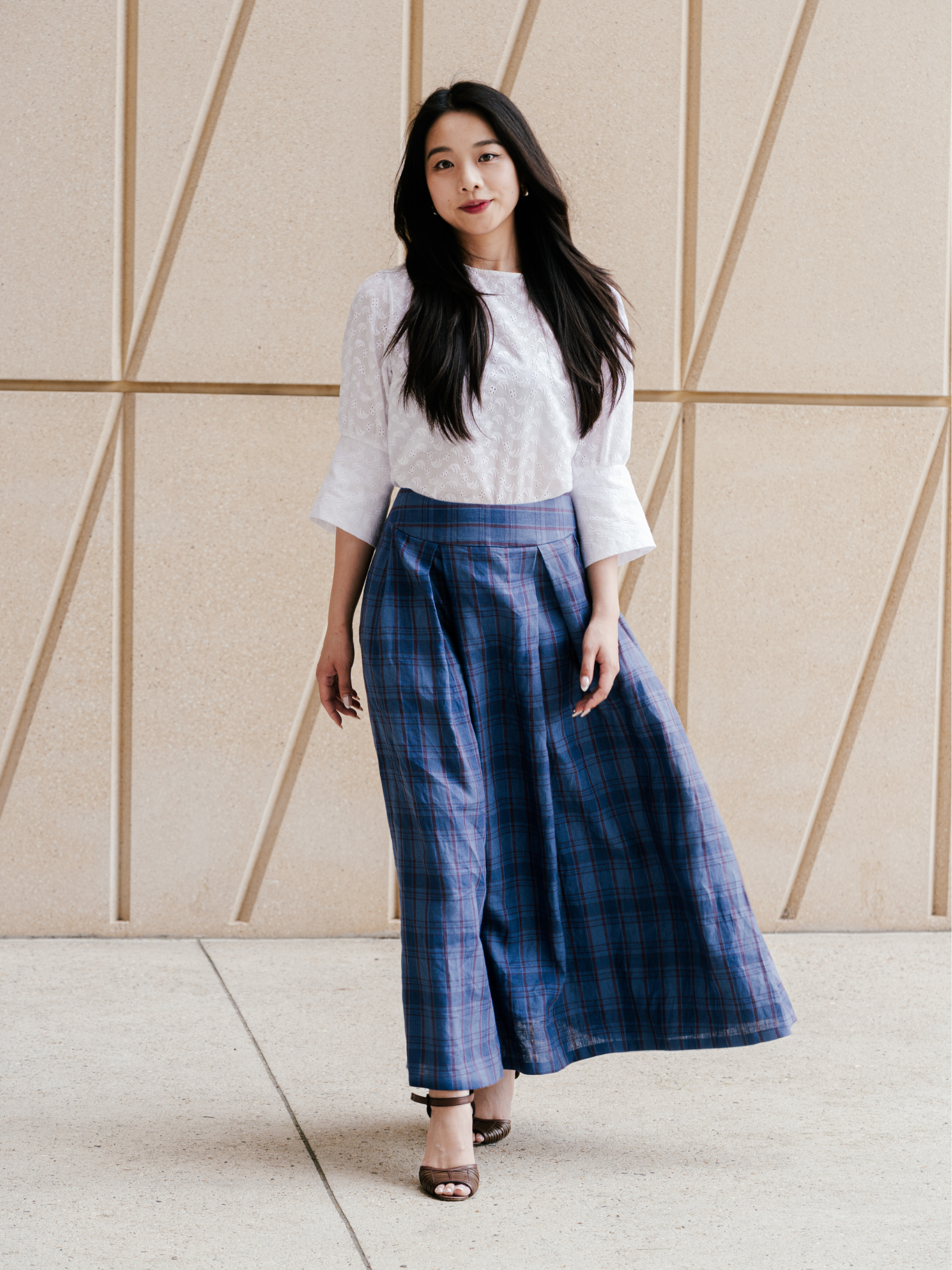 Woman wearing a white blouse and blue plaid skirt standing against a geometric wall.