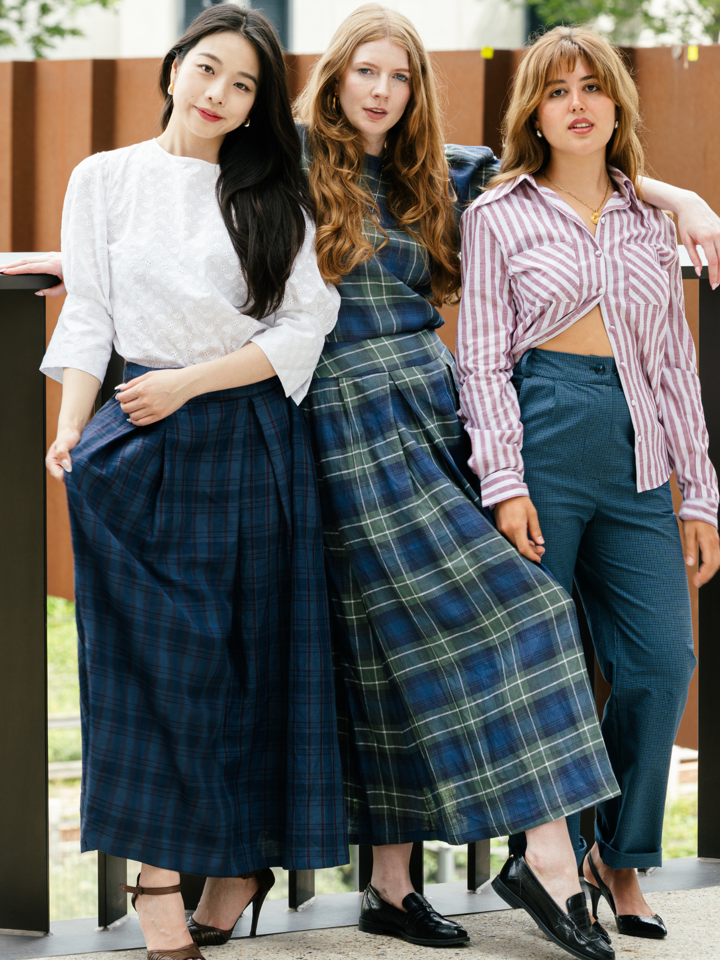 Three women standing together wearing plaid skirts and casual tops.