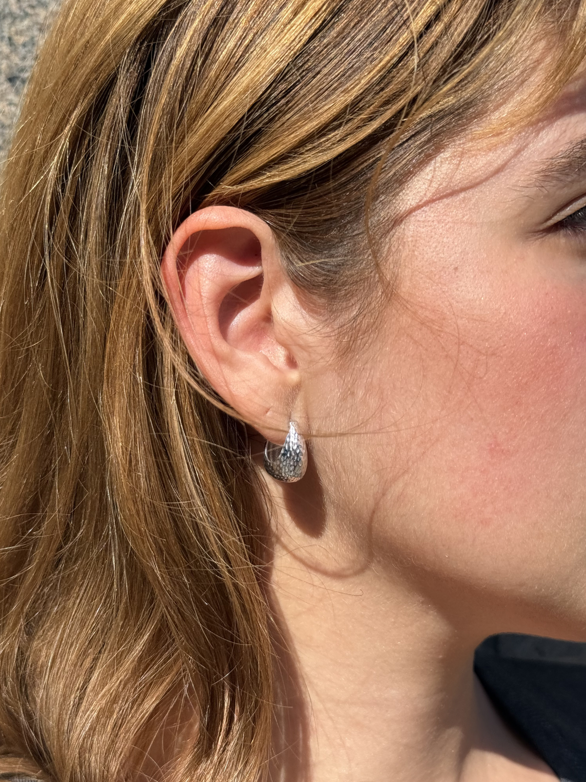 close up of a woman wearing silver textured small hoop earrings