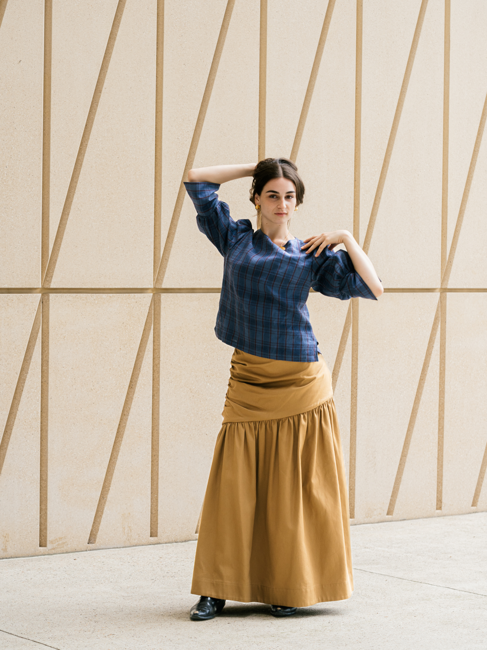 Woman wearing a blue top and brown skirt against a geometric wall.