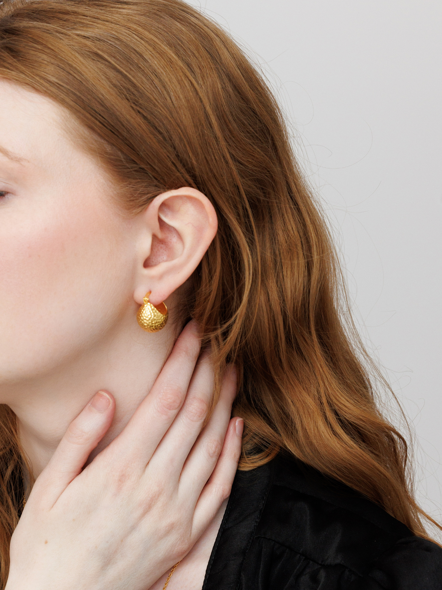 Close-up of a person wearing gold ball hoop earrings with a neutral background