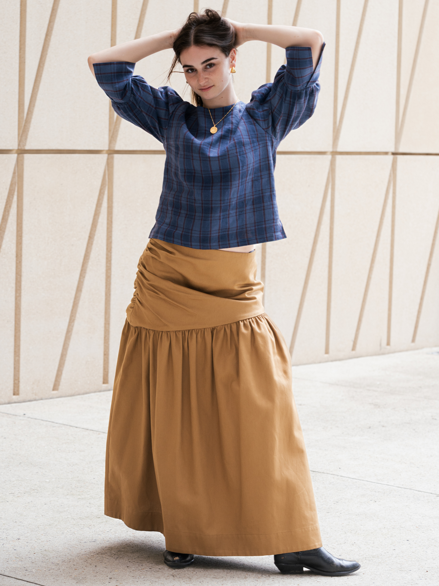 Woman wearing a blue plaid top and tan skirt against a neutral background