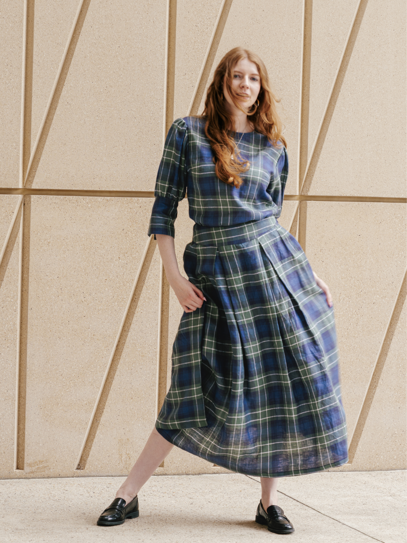 Woman wearing a blue and green plaid dress standing against a geometric wall.
