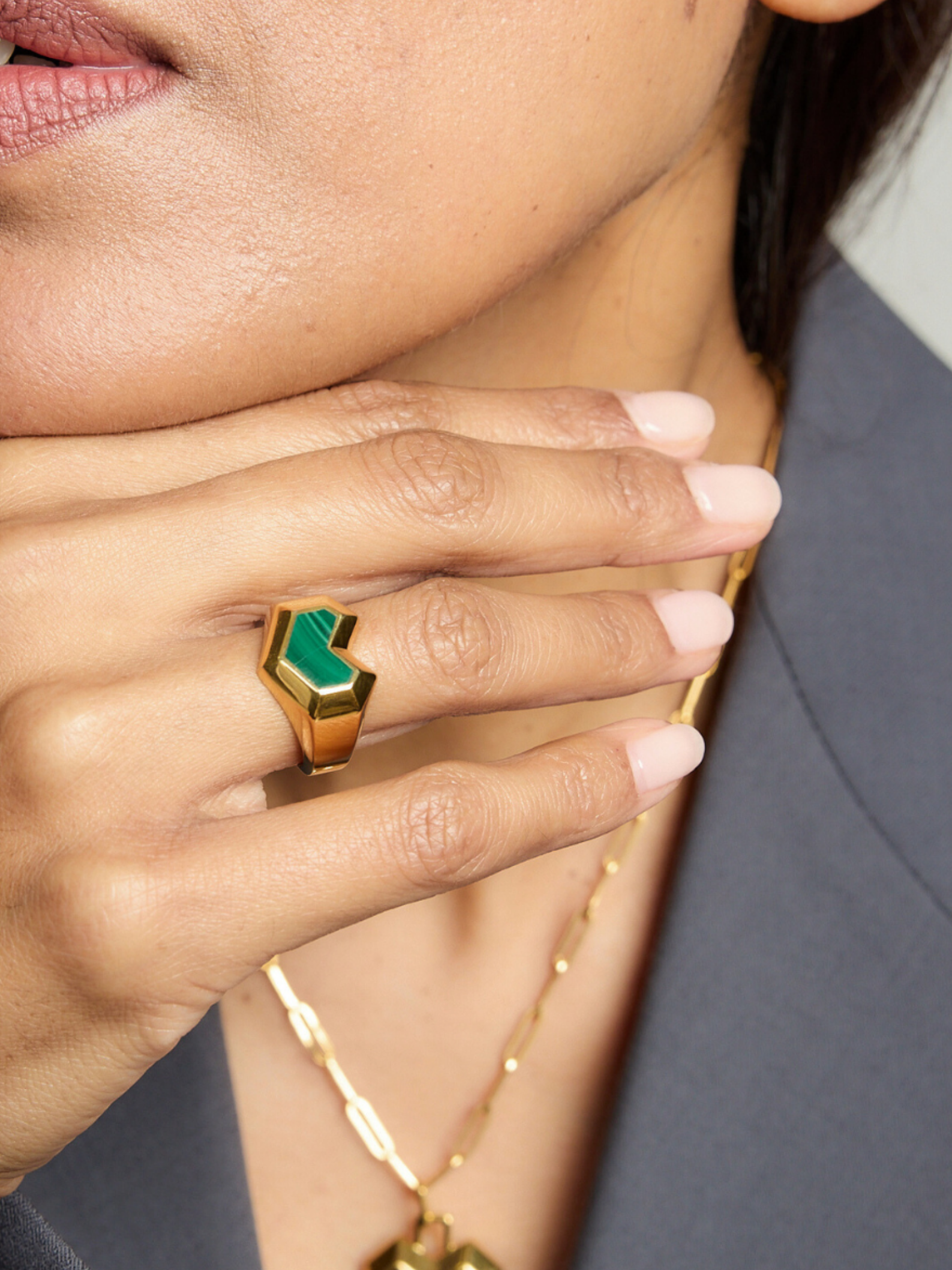 Close-up of a hand wearing a gold ring with a green stone, with a blurred background.