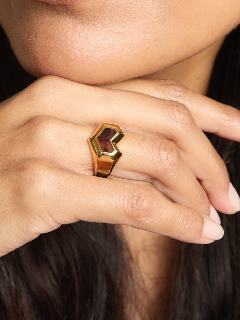 Close-up of a hand wearing a gold heart ring with a gemstone on a dark background