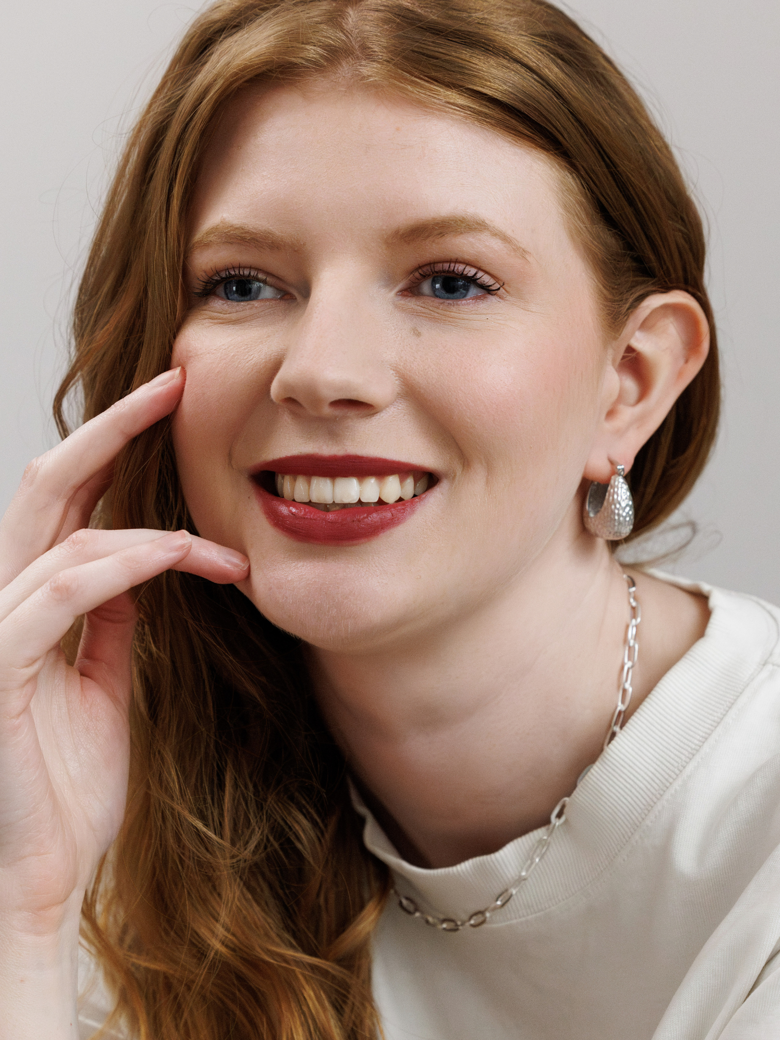 Woman wearing silver earrings and chain necklace against a neutral background
