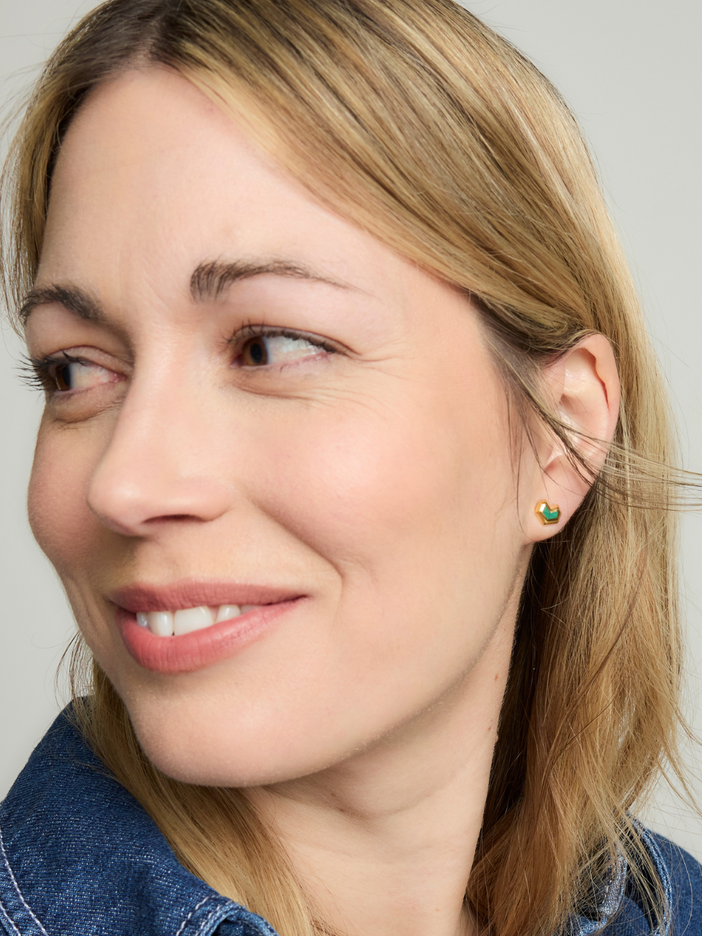 Close-up of a woman wearing a green stud earring against a neutral background