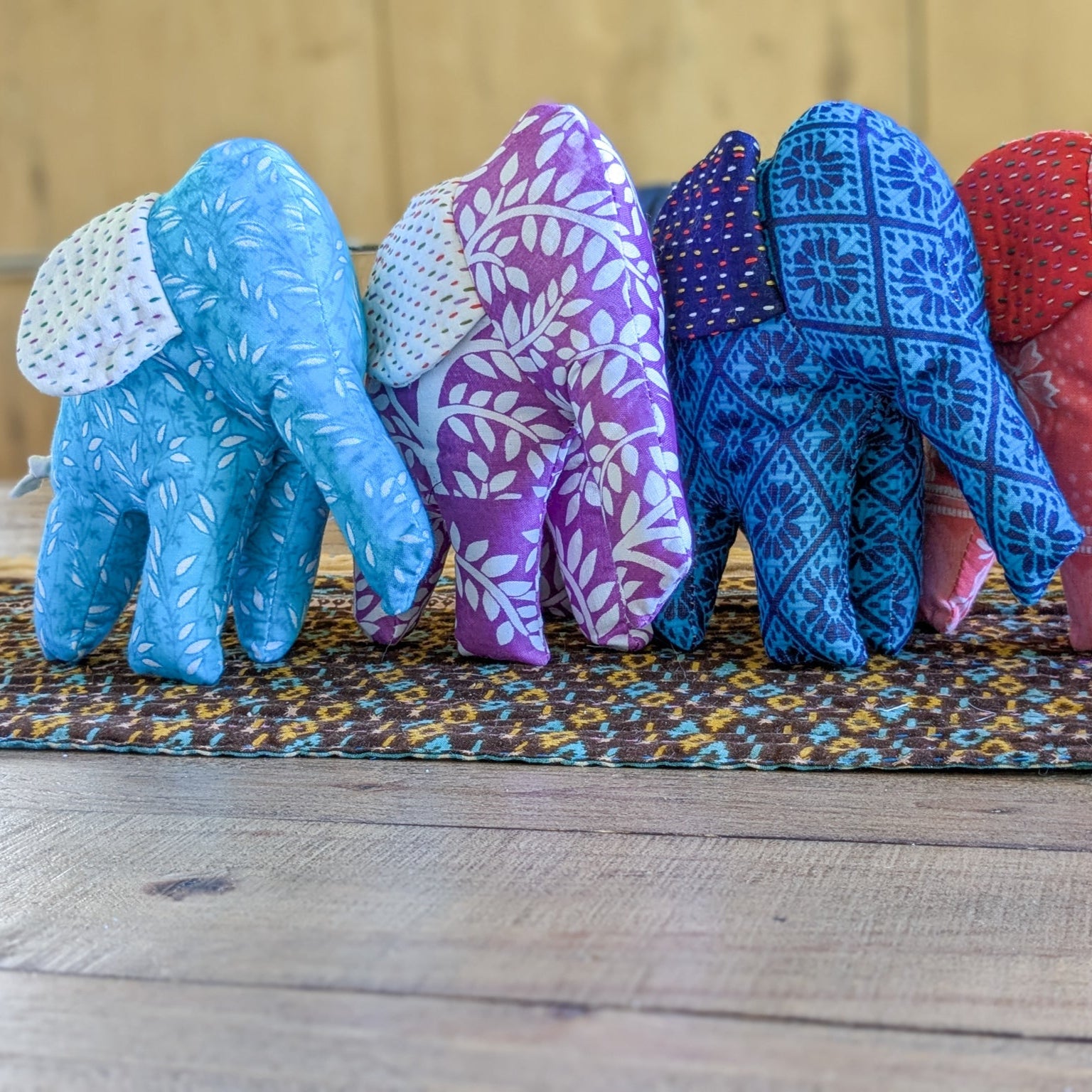 Fabric elephants of different colours arranged on a patterned mat.