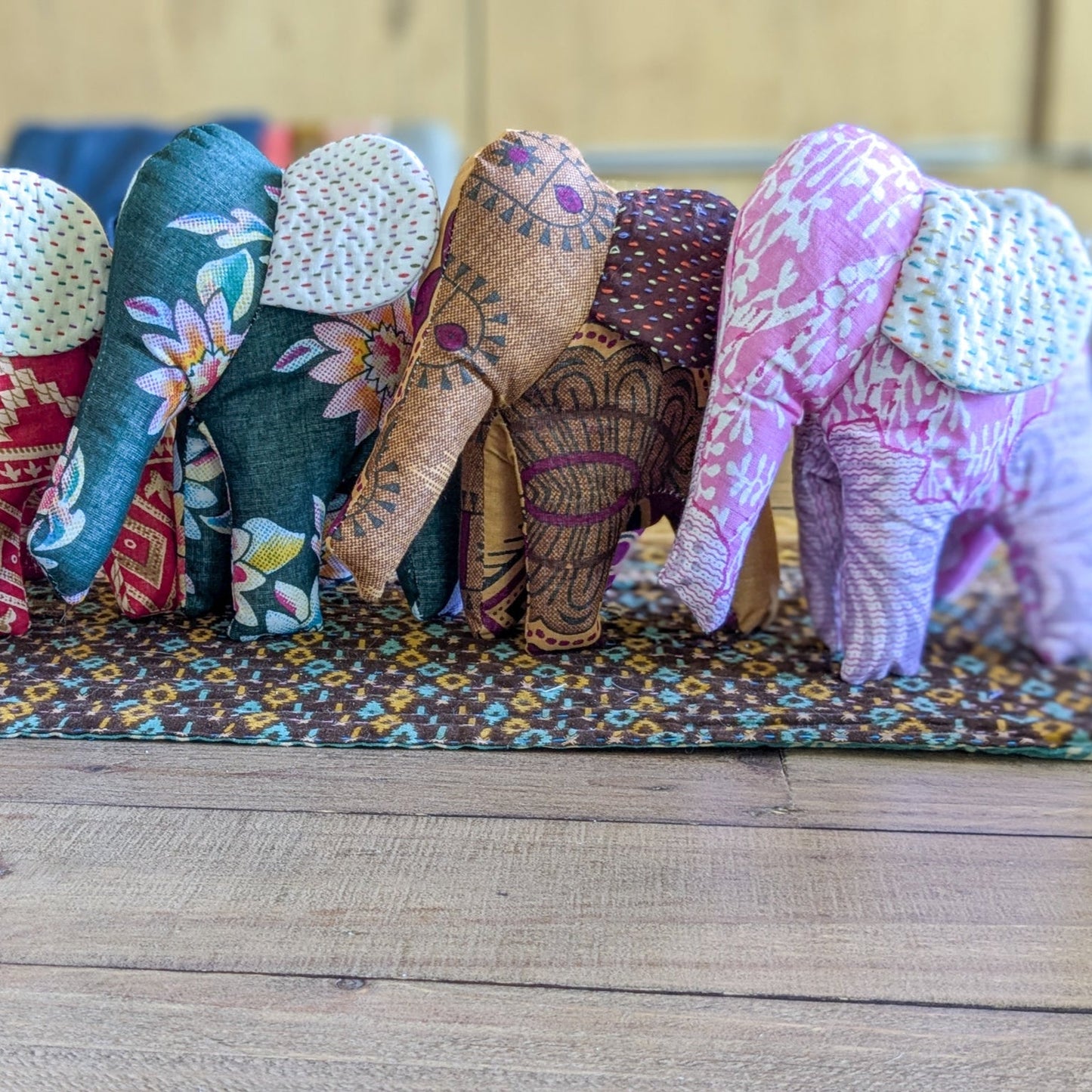 Colorful fabric elephants on a wooden surface with a patterned mat underneath.