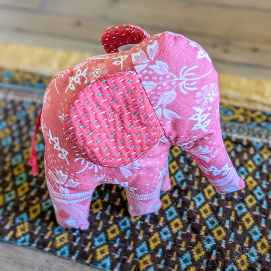 Pink fabric elephant on a colourful patterned surface