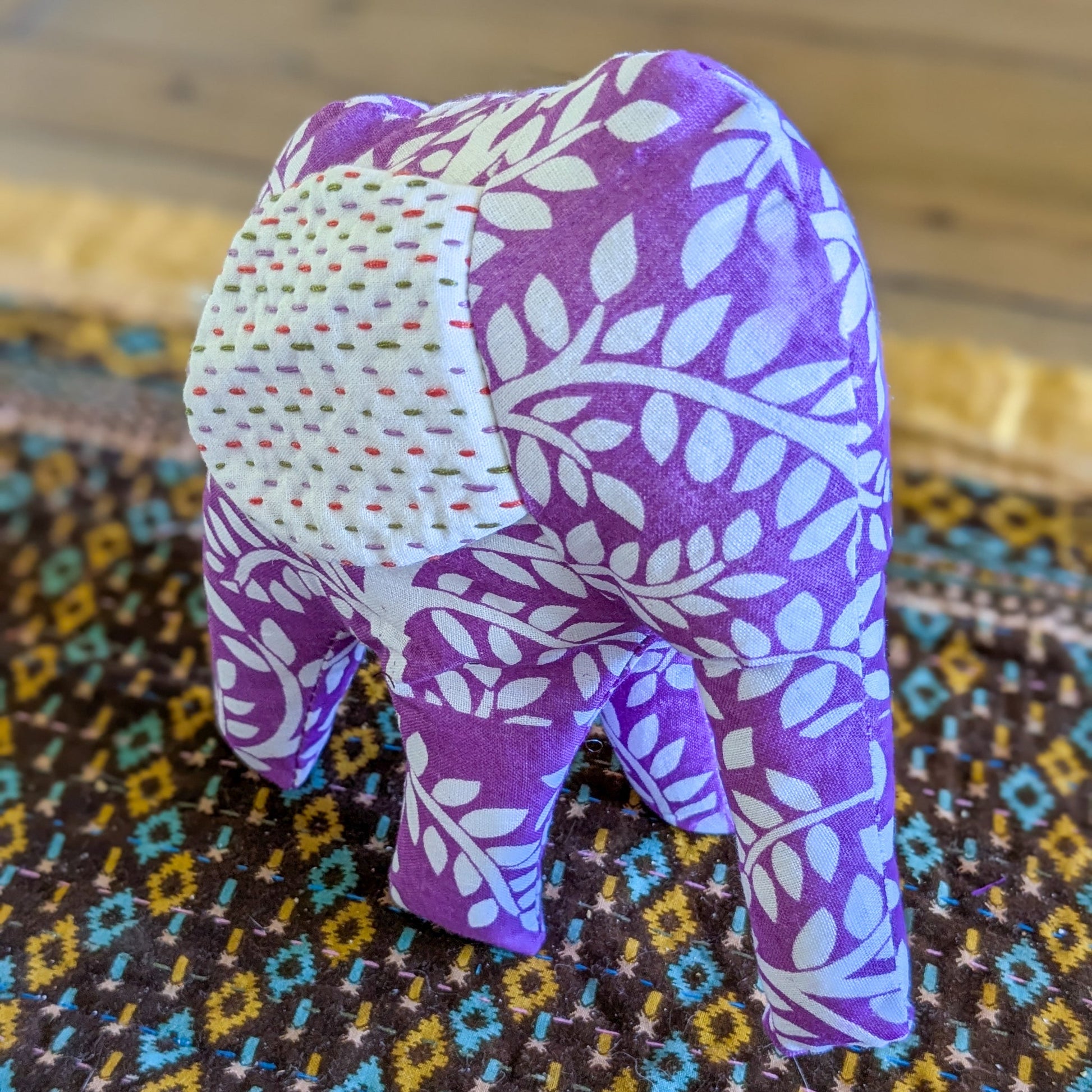 Purple fabric elephant with white patterns on a colorful patterned surface