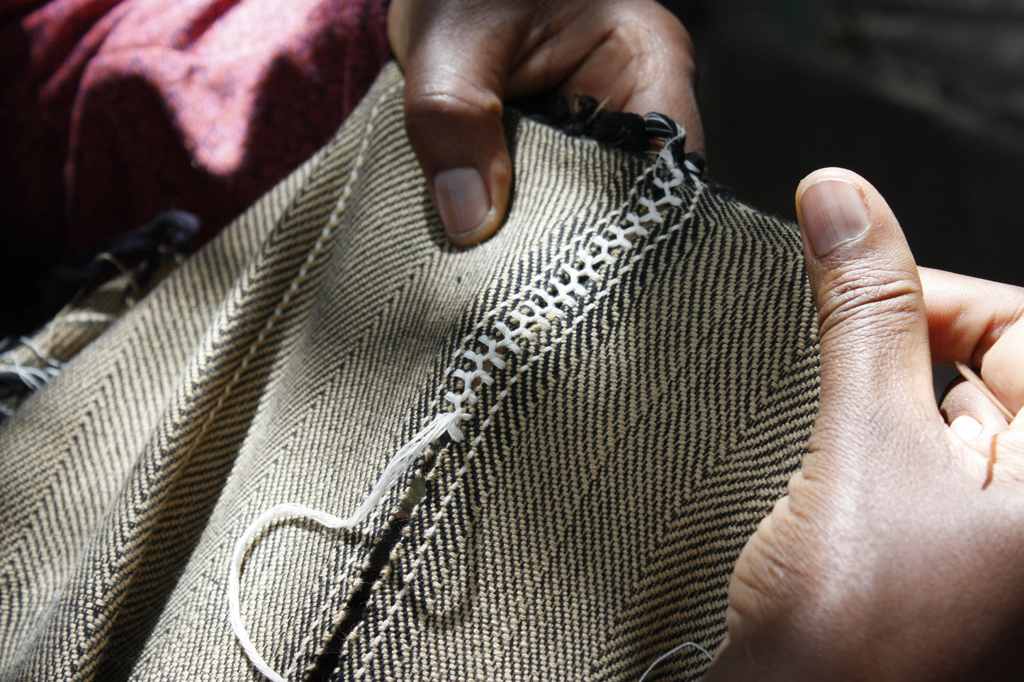 Close-up of hands sewing anna cape with a needle and thread.