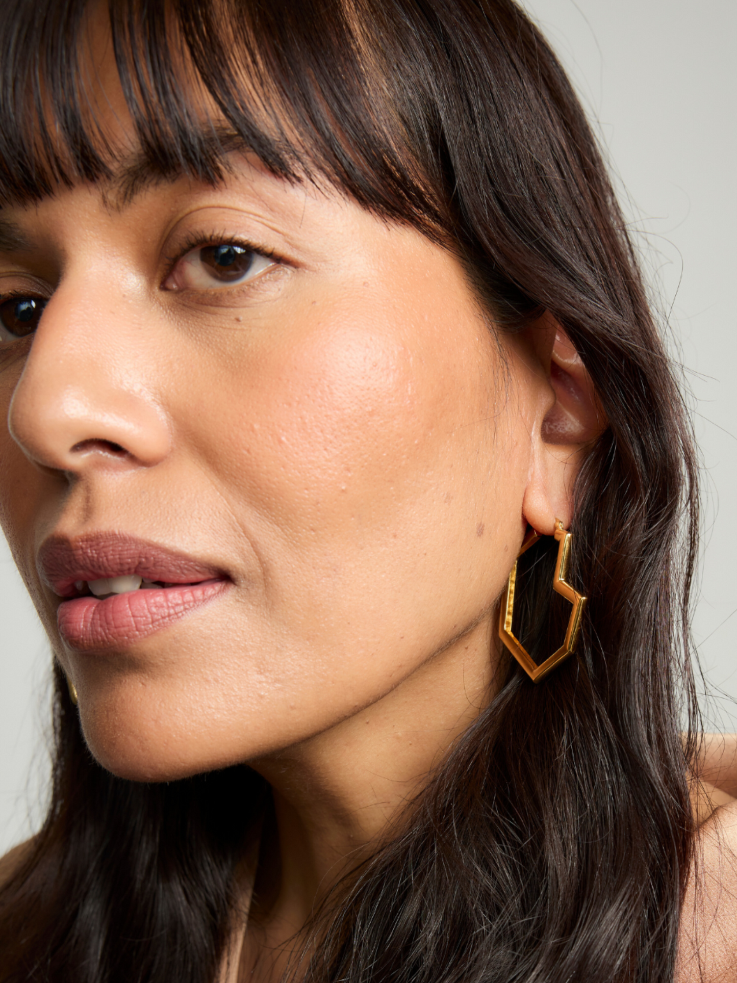 Close-up of a woman wearing gold hoop earrings with a neutral background