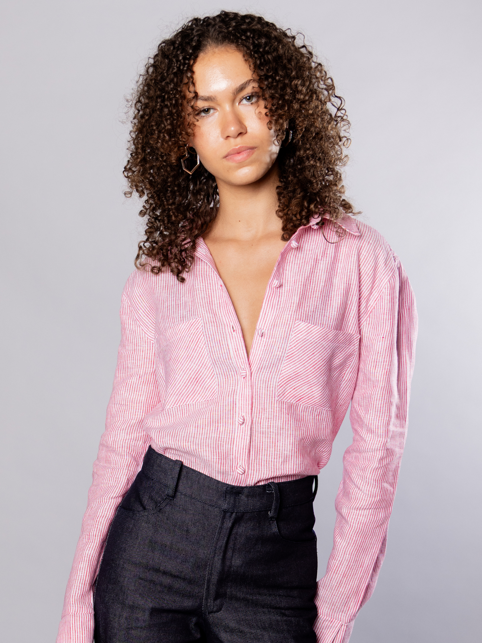 Woman wearing a red stripe shirt with silver heart hoop earrings against a grey background