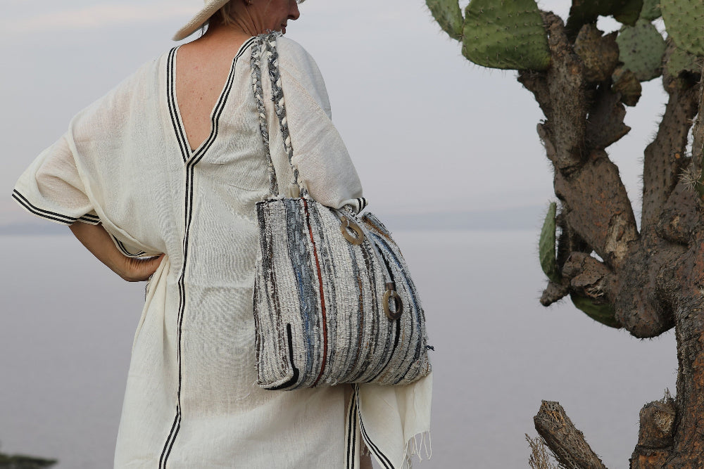 Woman in a petra kaftan and hat holding a patterned bag next to a cactus