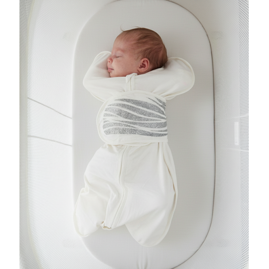 Newborn baby sleeping in a Sleep of Mind breathing reassurance swaddle in a white bassinet 