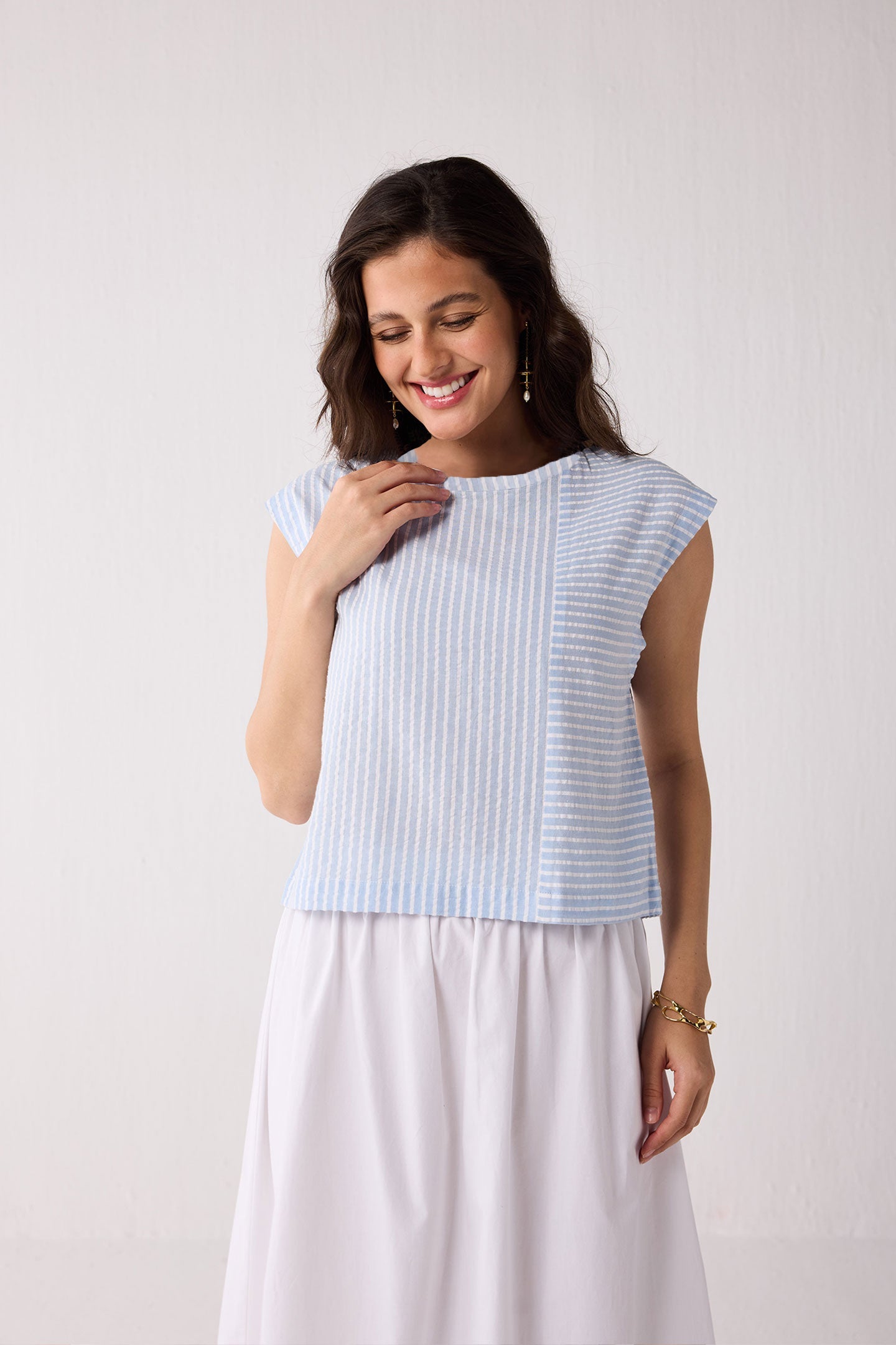 A woman wearing a light blue striped top and white skirt against a plain background