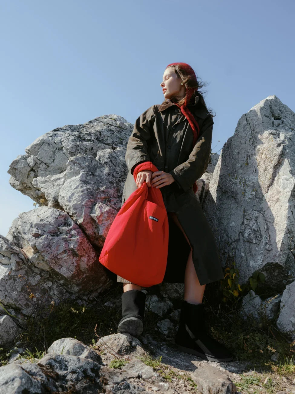 Person holding a red bag on rocky terrain with a clear blue sky