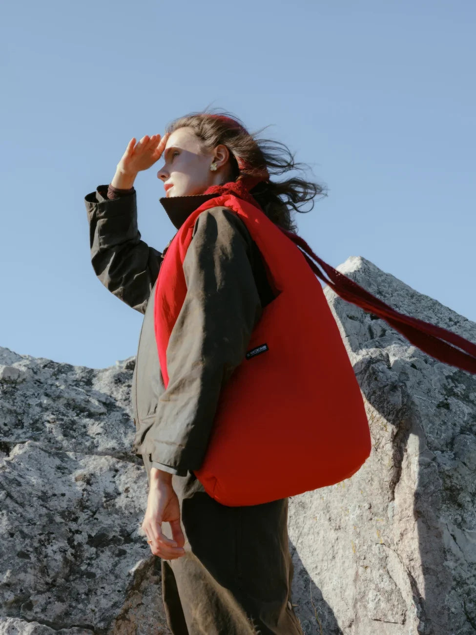 Person with a red bag standing on rocky terrain against a clear blue sky