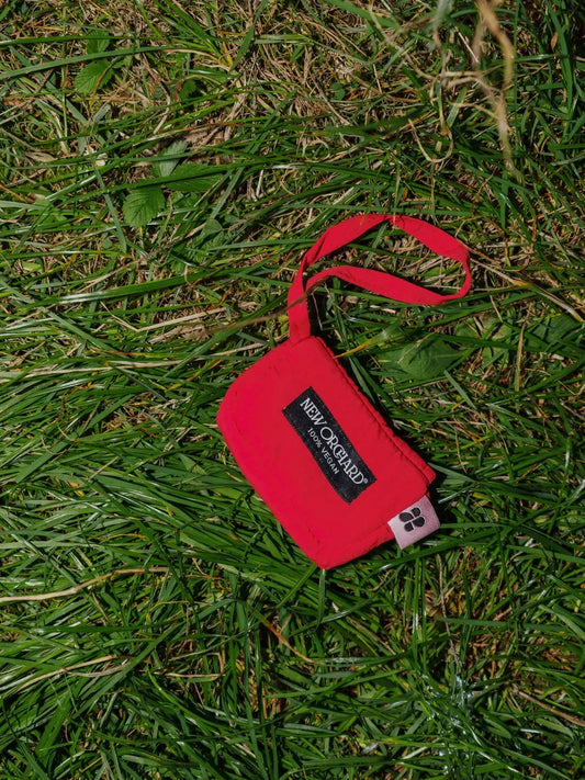 Vivid red vegan snack pouch made from recycled materials with wrist strap on grass background. - The New Orchard - Vivid Red