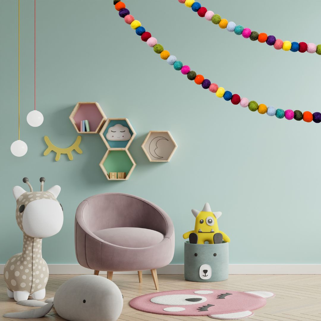 Children's room with a pink chair, colourful felt garland decor, and toys on a light green wall.