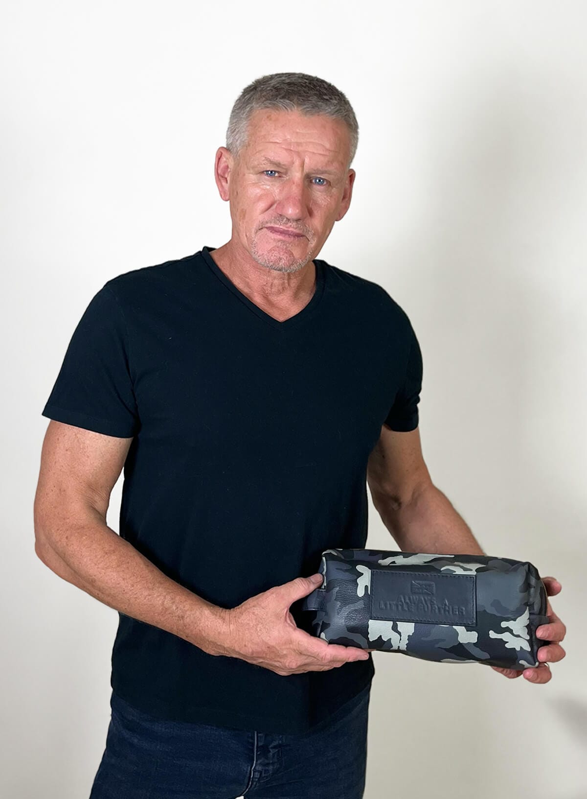 Man holding a camouflage-patterned toiletry bag against a white background