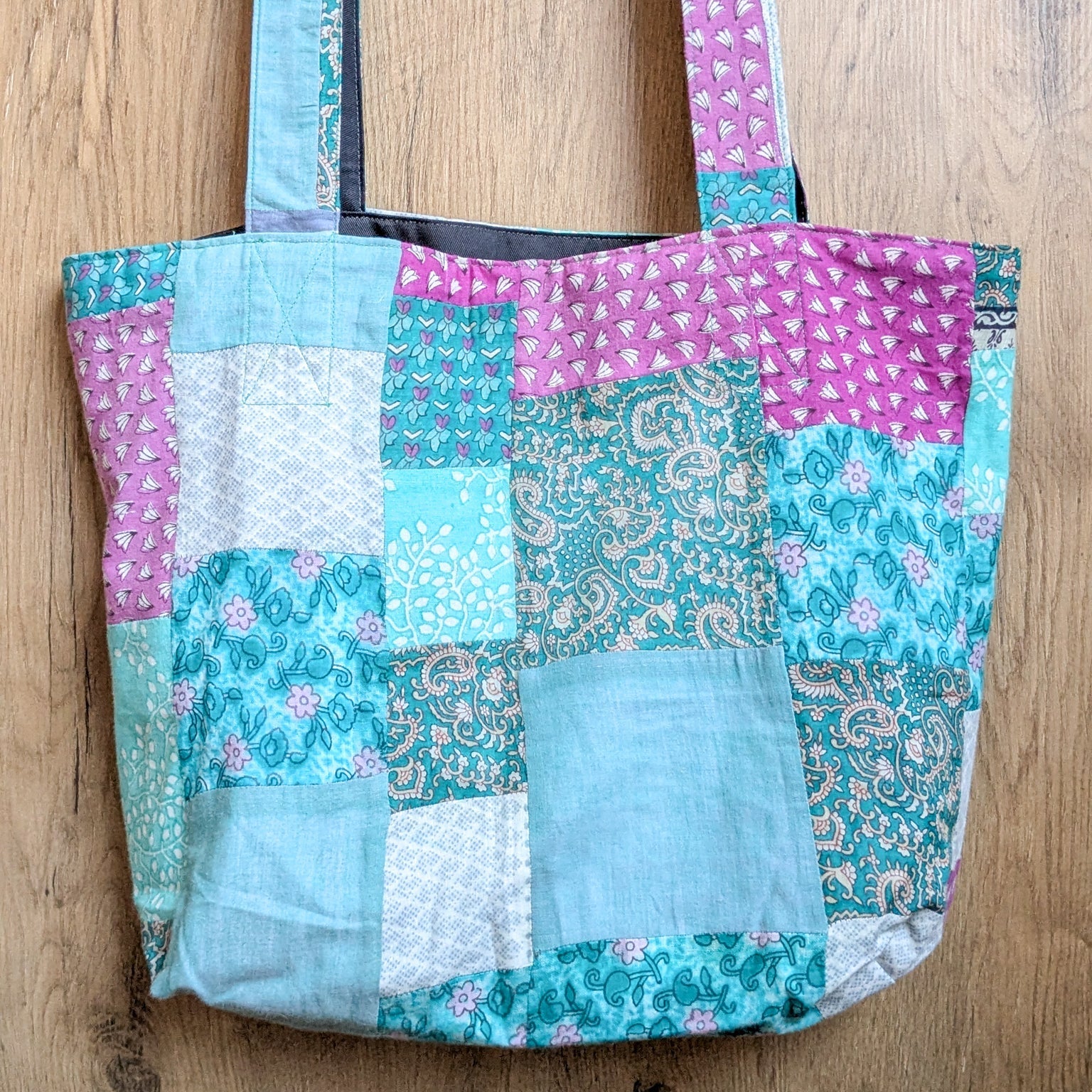 Patchwork tote bag with floral and paisley patterns on a wooden surface