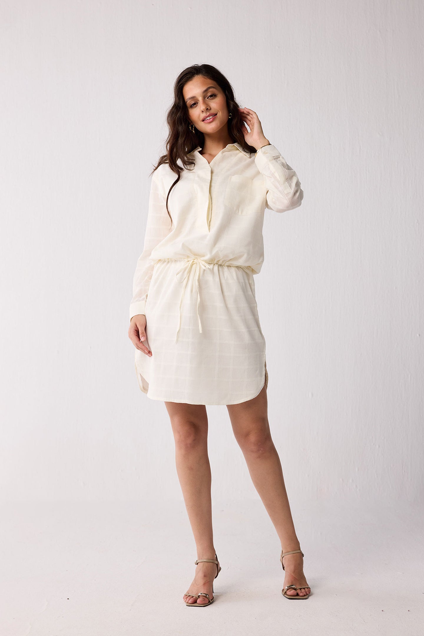 Woman wearing a white dress with a belt against a plain background