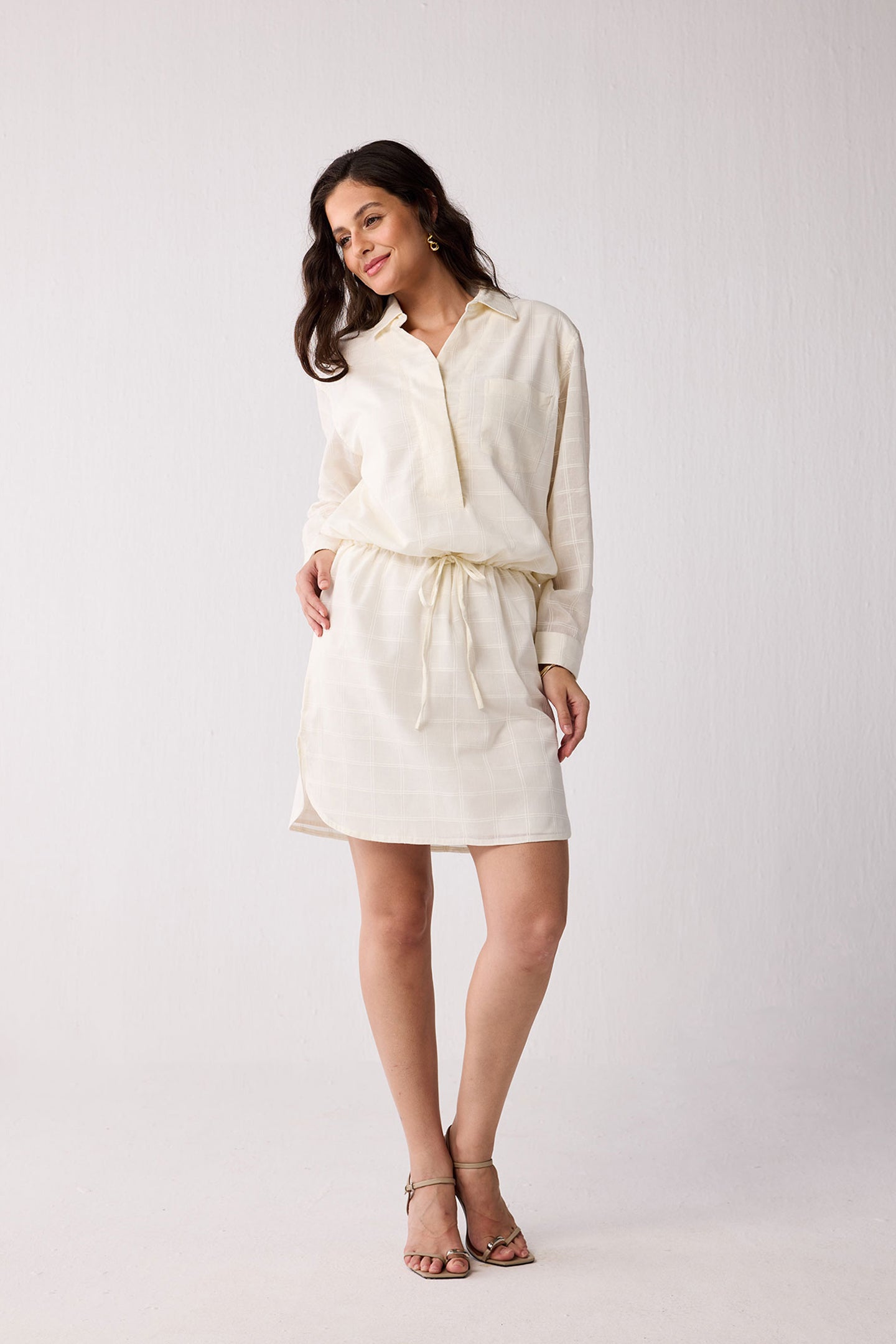 Woman wearing a cream-colored dress with a belt on a white background