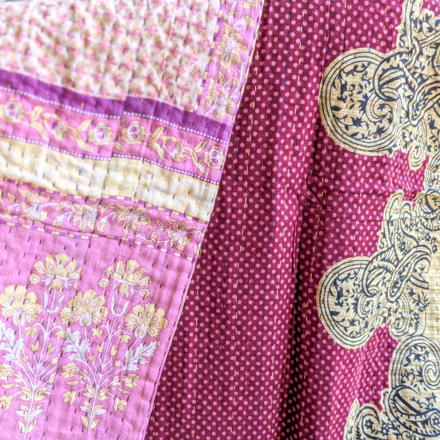 Close-up of a pink and yellow patterned fabric kantha quilt with intricate designs.