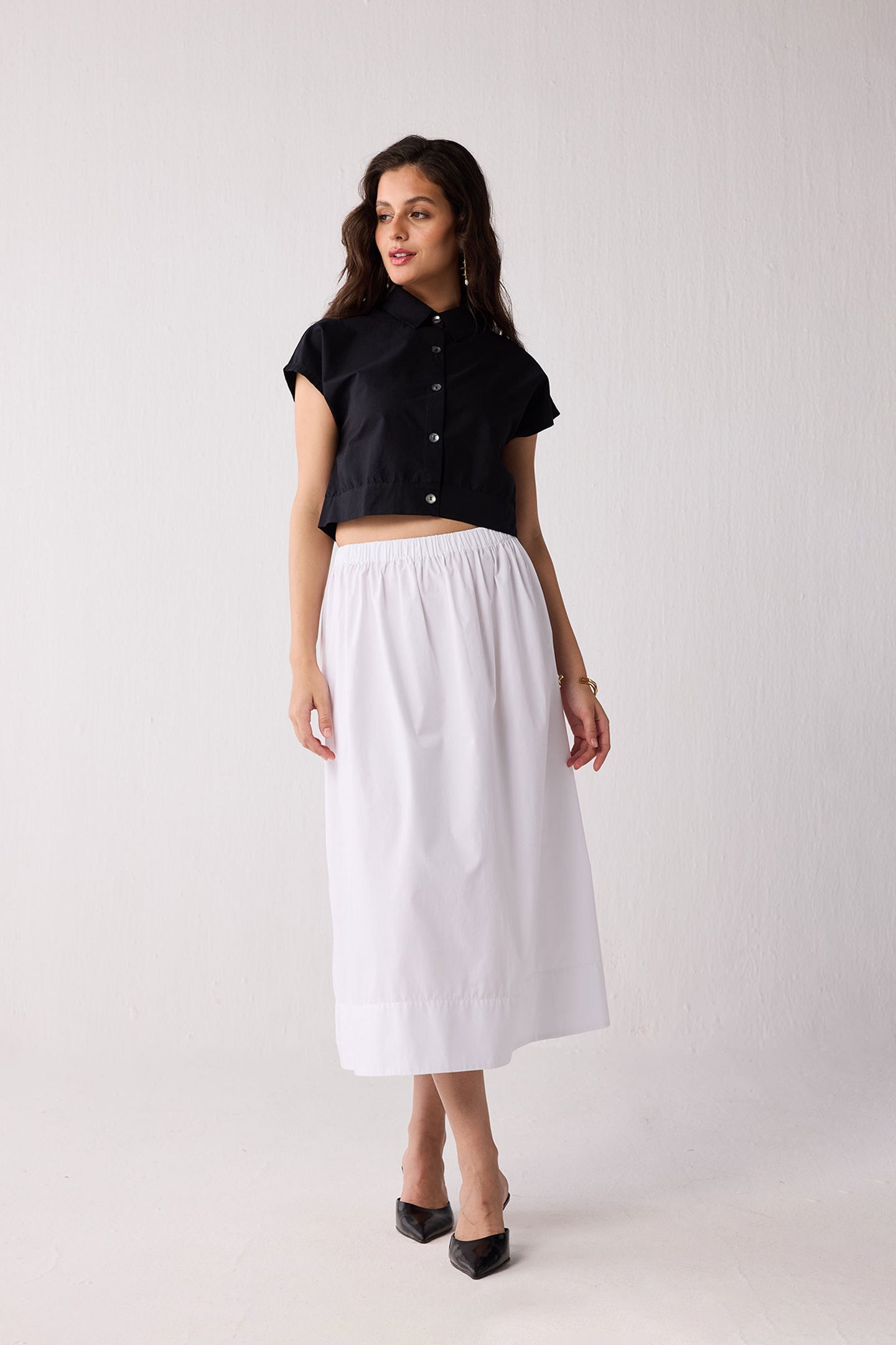 Woman wearing a black top and white skirt on a plain background