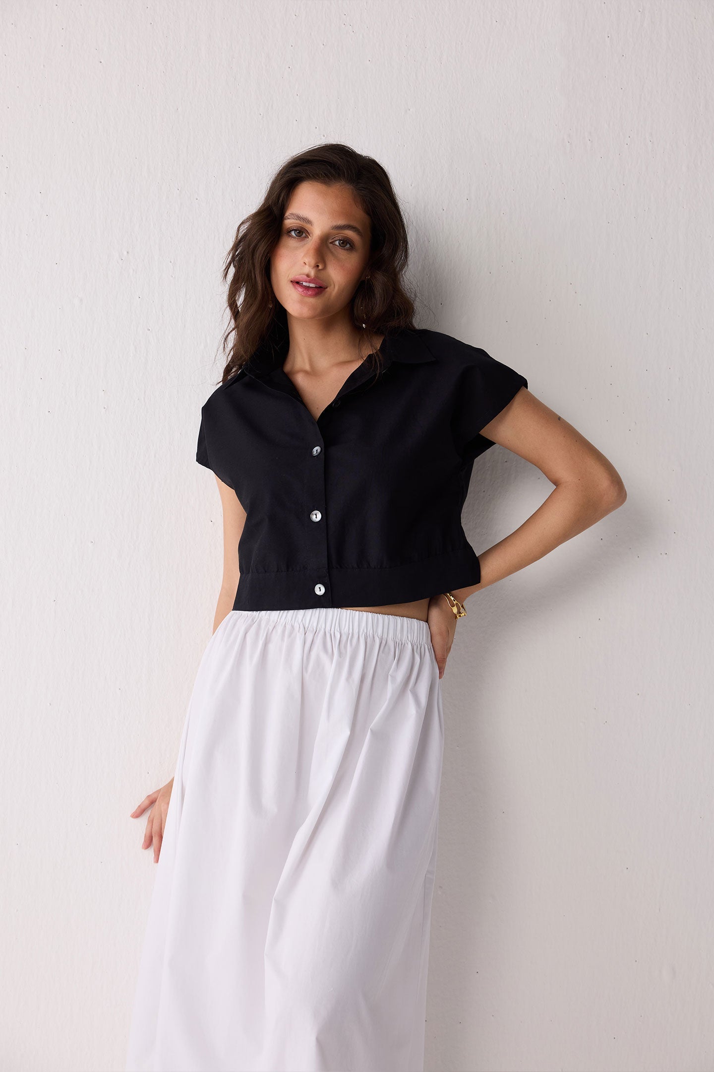 Woman wearing a black top and white skirt against a plain background