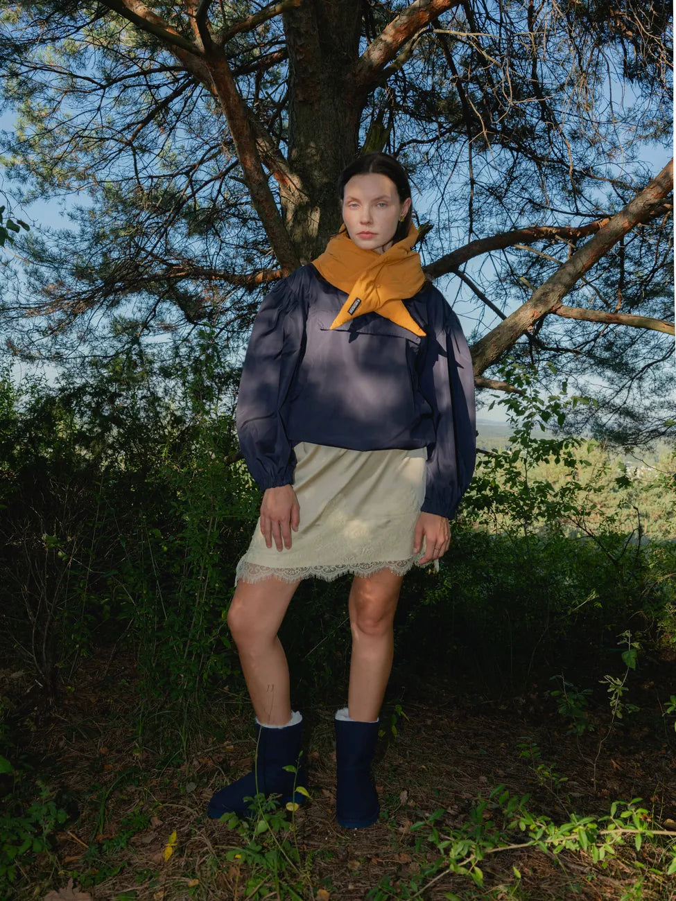 Man wearing amber yellow vegan scarf made from recycled materials with navy sweater and beige skirt outdoors under tree. - The New Orchard - Amber Yellow