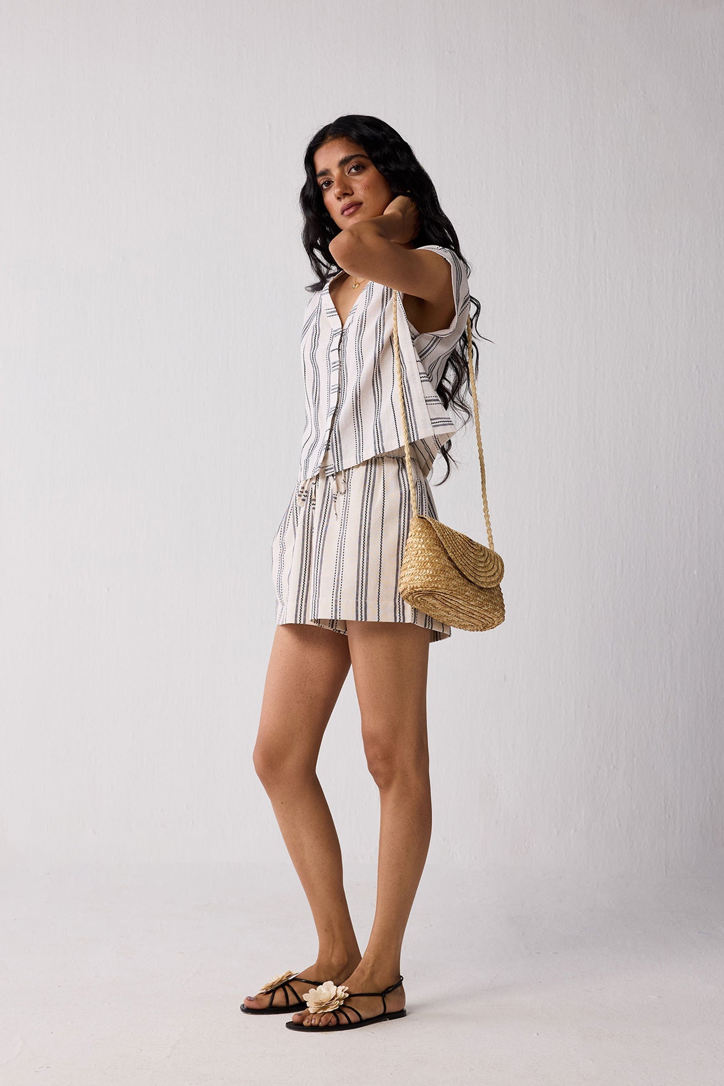 Woman in a striped outfit holding a straw bag against a plain background