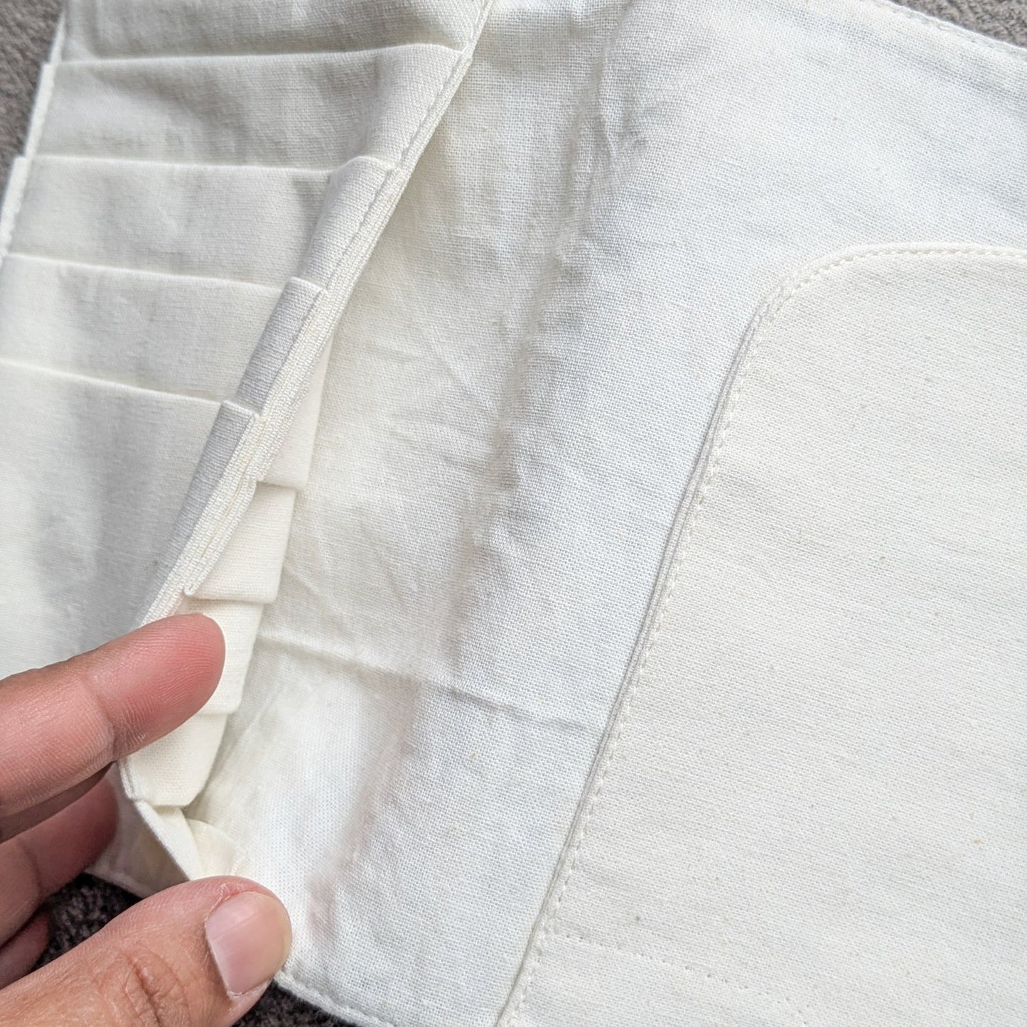 Close-up of a white fabric pocket with a hand holding it open on a grey background