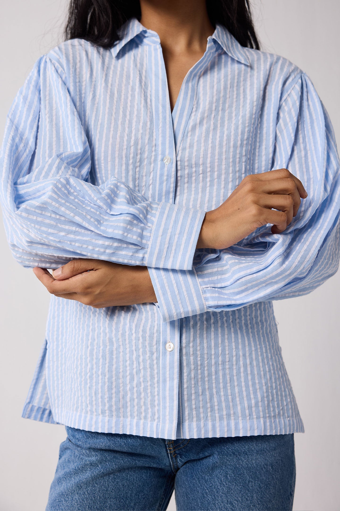 Woman wearing a light blue striped shirt and jeans on a white background