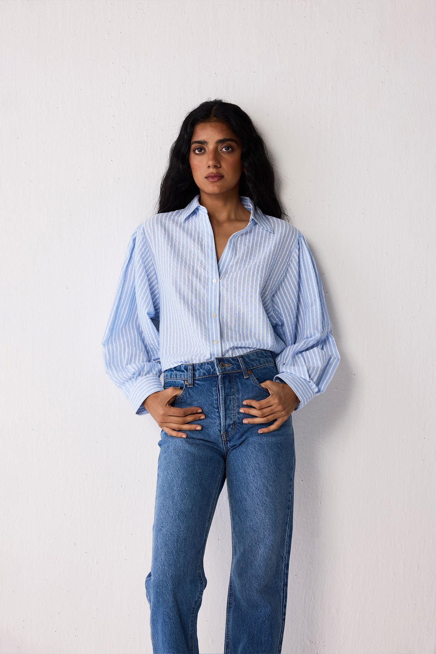 Woman wearing a light blue striped shirt and jeans on a white background