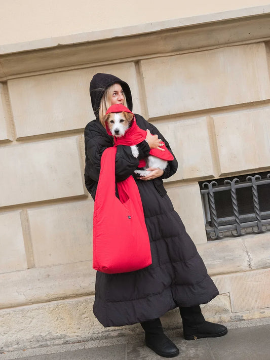 Person wearing a black skirt with a small dog, standing against a beige wall.