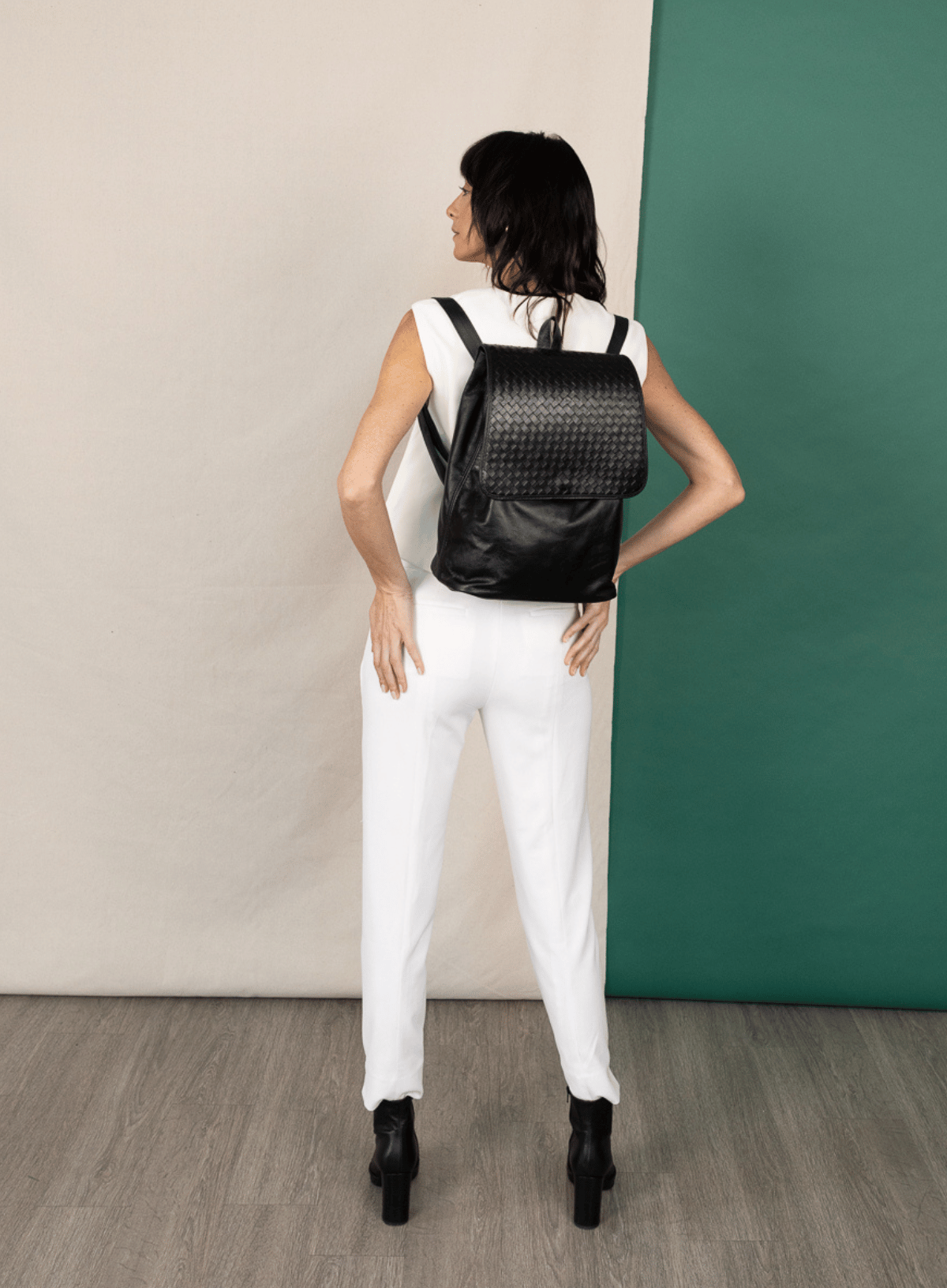 model standing wearing black woven backpack infront of white and green background